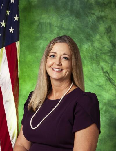 Shelly Scott posing in front of green background and U.S. flag. 